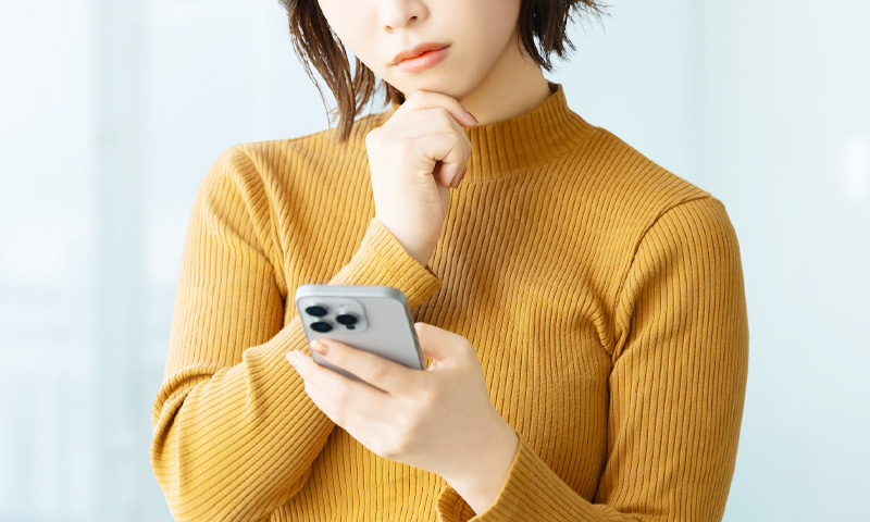 スマホを眺めてながら悩む女性のイメージ写真